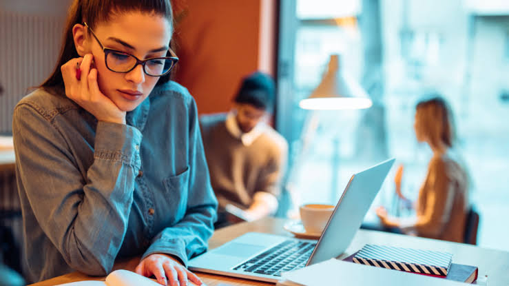 A girl studying from a book with a laptop in front of her