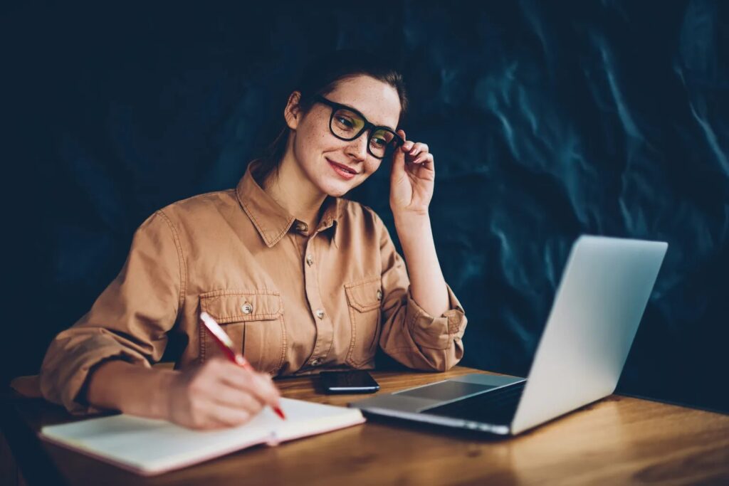 Lady writing on a book from a laptop. 